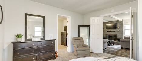 A bedroom with a large bed, a dresser, a chair, and a TV in the adjacent living area.