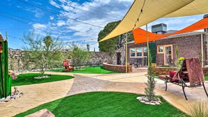 A patio area with a stone pathway, green lawn, outdoor furniture, and a building with a brick facade.