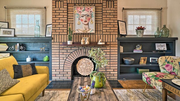 A living room with a brick fireplace, a yellow sofa, a floral armchair, and a coffee table with decorative items.