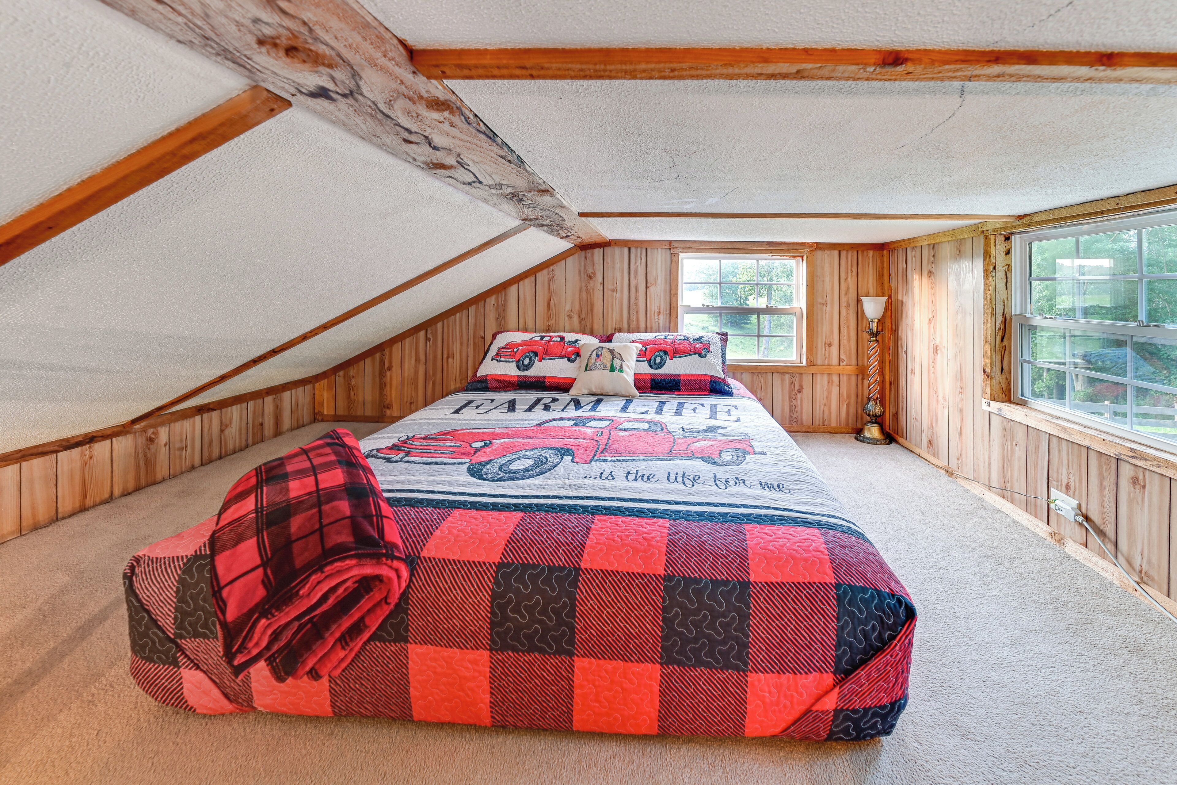 Une chambre confortable située sous les toits, avec des murs en bois, un plafond en pente et une grande fenêtre.