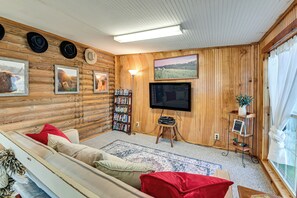 Ein gemütliches Blockhaus-Interieur mit einer Couch, roten Kissen, einem Flachbildfernseher, einem Bücherregal und gerahmten Bildern von Stieren.