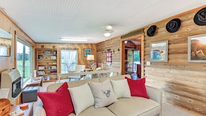 A cozy cabin interior with a beige sofa, red cushions, wooden walls, and a bookshelf filled with books and decorative items. - Cabin on Working Highland Cattle Farm in Kentucky (Annville)