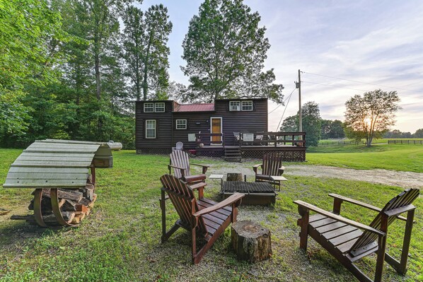 Eine rustikale Holzhütte mit einer Veranda, umgeben von einer Rasenfläche mit Adirondack-Stühlen und einer Feuerstelle.