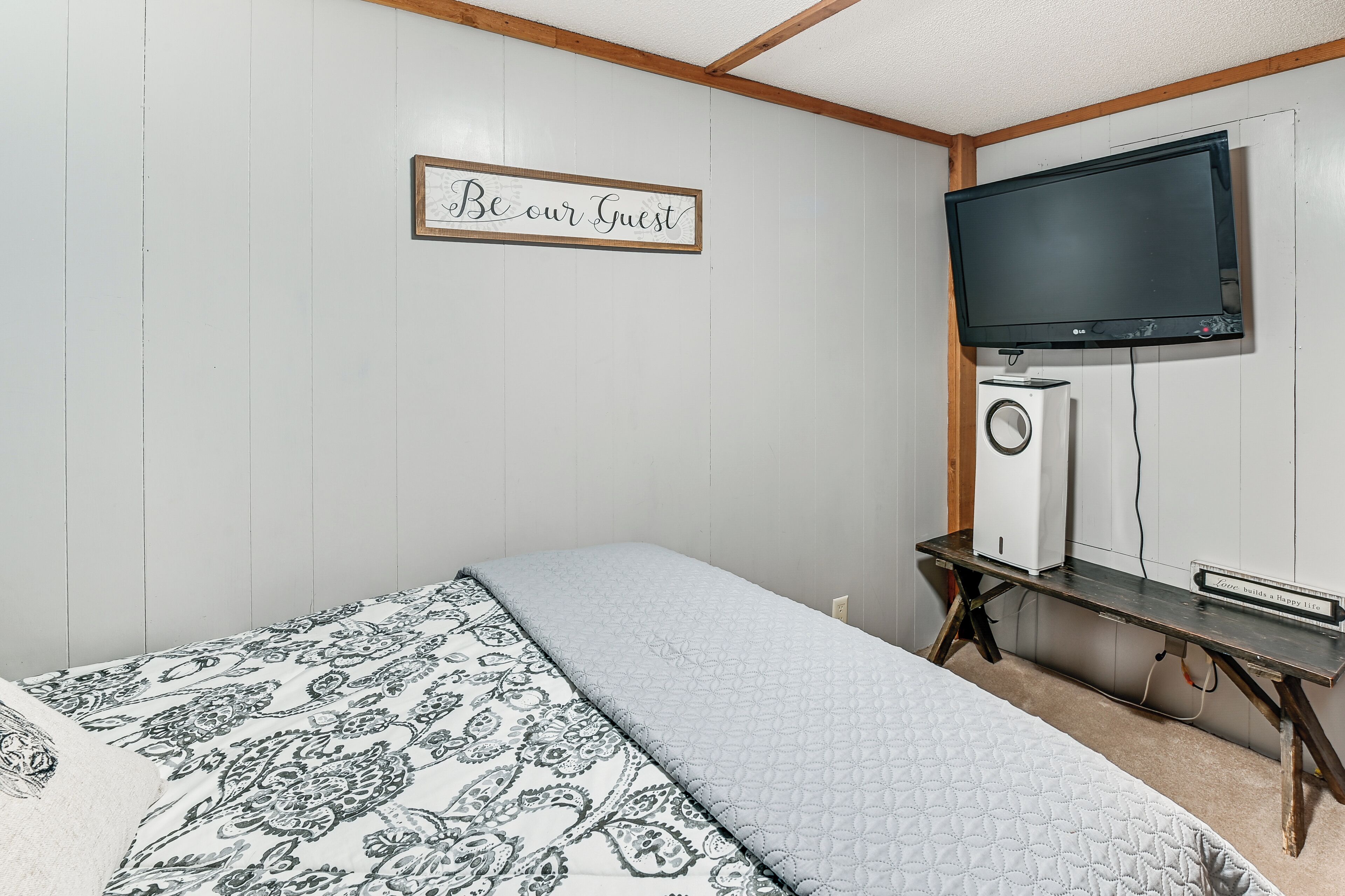 A bedroom with a bed, a TV mounted on the wall, and a small table with a speaker.