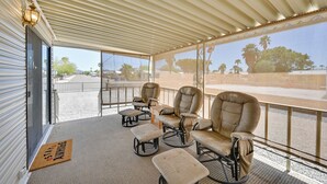A covered outdoor seating area with cushioned chairs and ottomans, a doormat with text, and a view of a road and trees. - Pet-friendly Vacation Rental in Yuma With Grill! (Yuma)