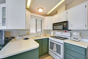 Una cocina con armarios blancos, estufa, microondas y cafetera.