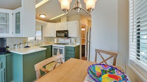 A compact kitchen with white cabinets, a microwave, a stove, and a dining area with a wooden table and chairs. - Pet-friendly Vacation Rental in Yuma With Grill! (Yuma)