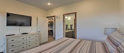 Un dormitorio con cama, cómoda, televisor y puerta que da a un baño.