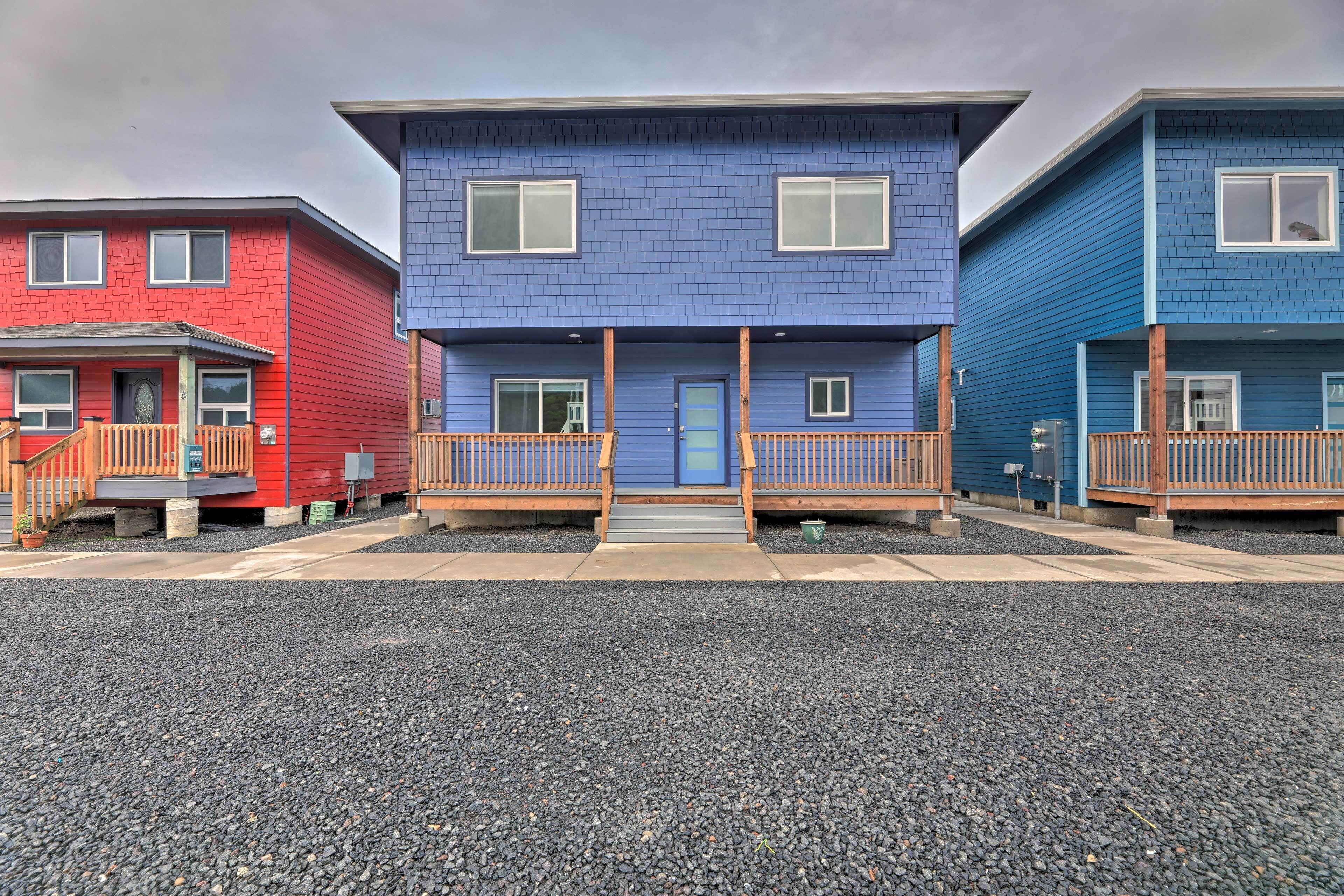 Une rangée de trois maisons de ville, avec une maison bleue au centre, flanquée de maisons rouges et bleues, chacune dotée d’un balcon en bois et d’une porte d’entrée.