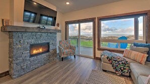 A modern living room with a stone fireplace, a comfortable sofa, and large windows offering a view of the outdoors. - Sanderling Sea Cottages, Unit 6 w/ Beach Access! (Waldport)