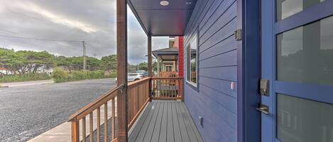 A wooden deck with a railing, a blue building with a glass door, and a clear sky.