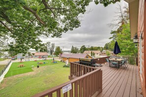 A deck with outdoor seating, a barbecue grill, and a view of a grassy area with tables and chairs. - Charming Curtis House: Large Deck w/ Lake View! (Curtis)