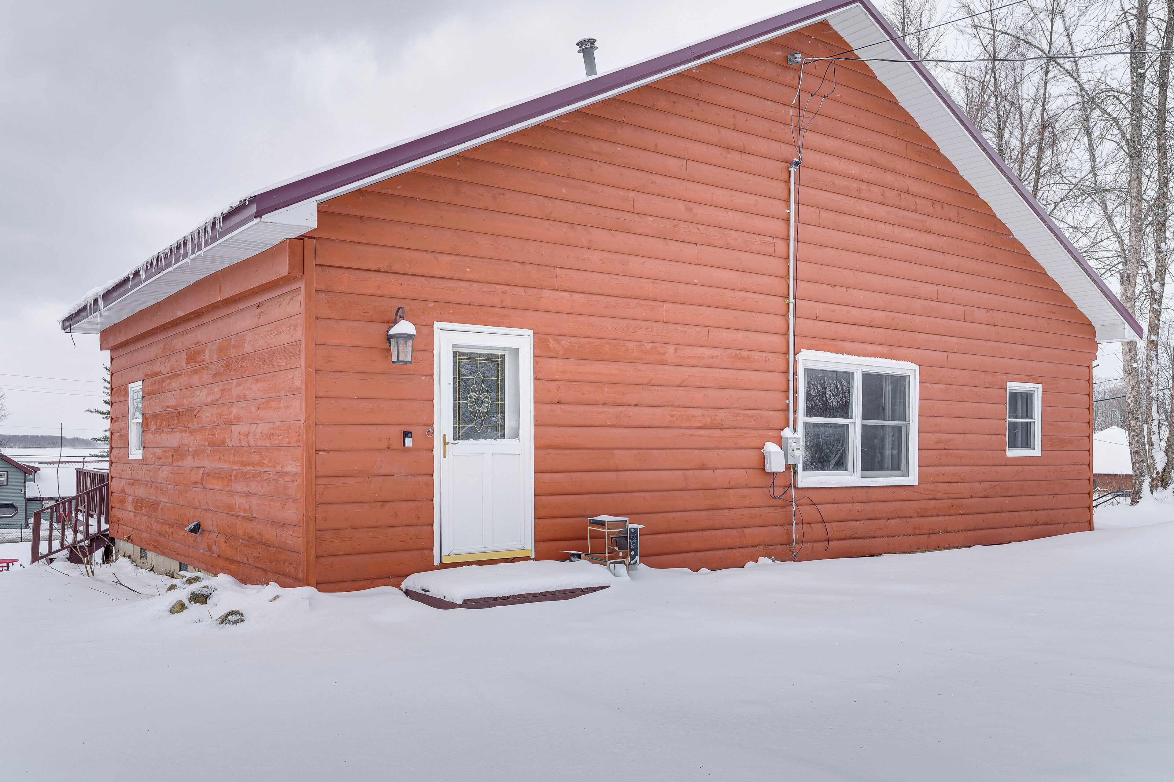A red wooden house with a white door, a small porch, and a snow-covered ground.