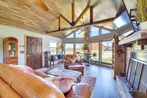 Un salón amplio con sofás de cuero, chimenea y ventanas grandes que ofrecen vistas al exterior.
