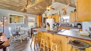 A kitchen with wooden cabinets, a central island with stools, a ceiling fan, and a deer head decoration.