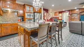 A kitchen with wooden cabinets, a granite countertop, a chandelier, and a dining area with chairs and a table. - Luxe Atwater Home w/ Patio: 10 Mi to Yosemite Lake (Atwater)