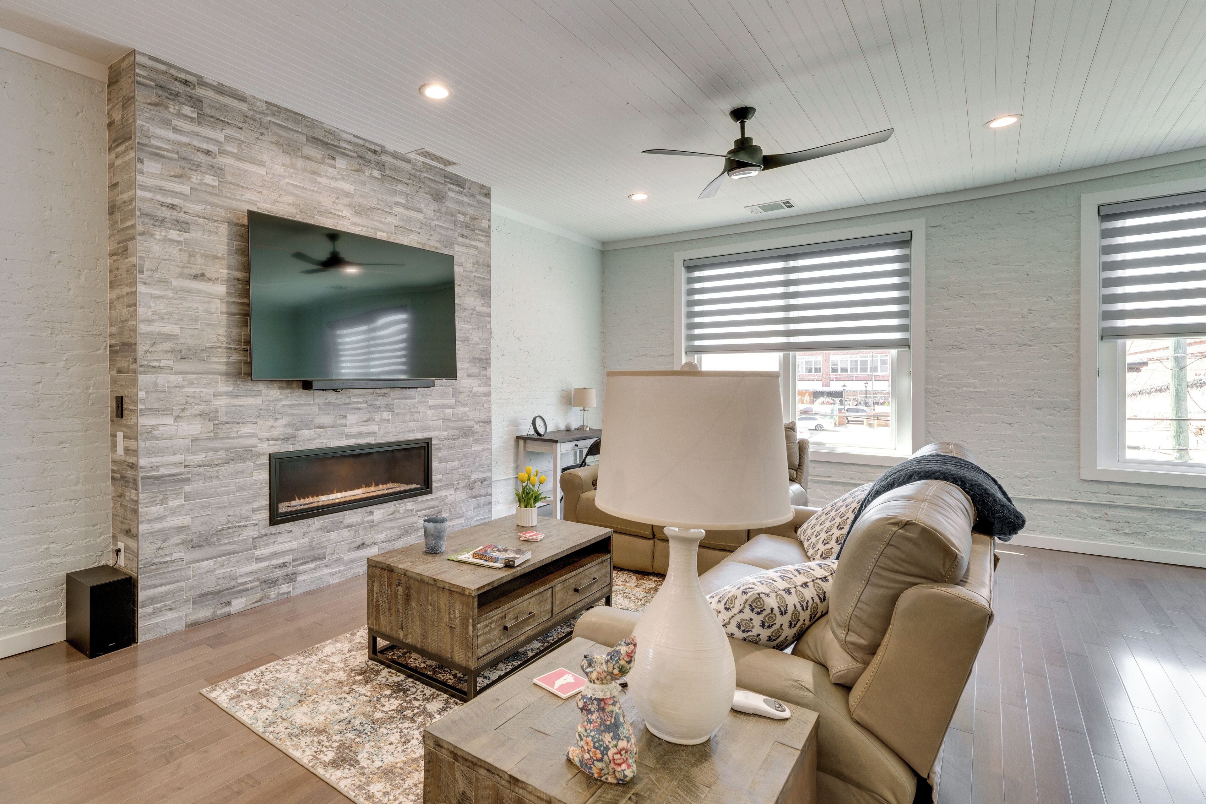 A modern living room with a stone wall, flat-screen TV, fireplace, and large windows.