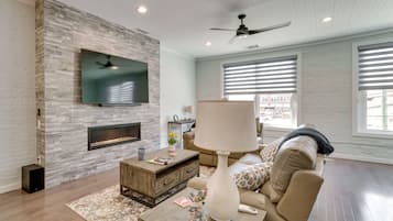 A modern living room with a stone wall, flat-screen TV, fireplace, and large windows.