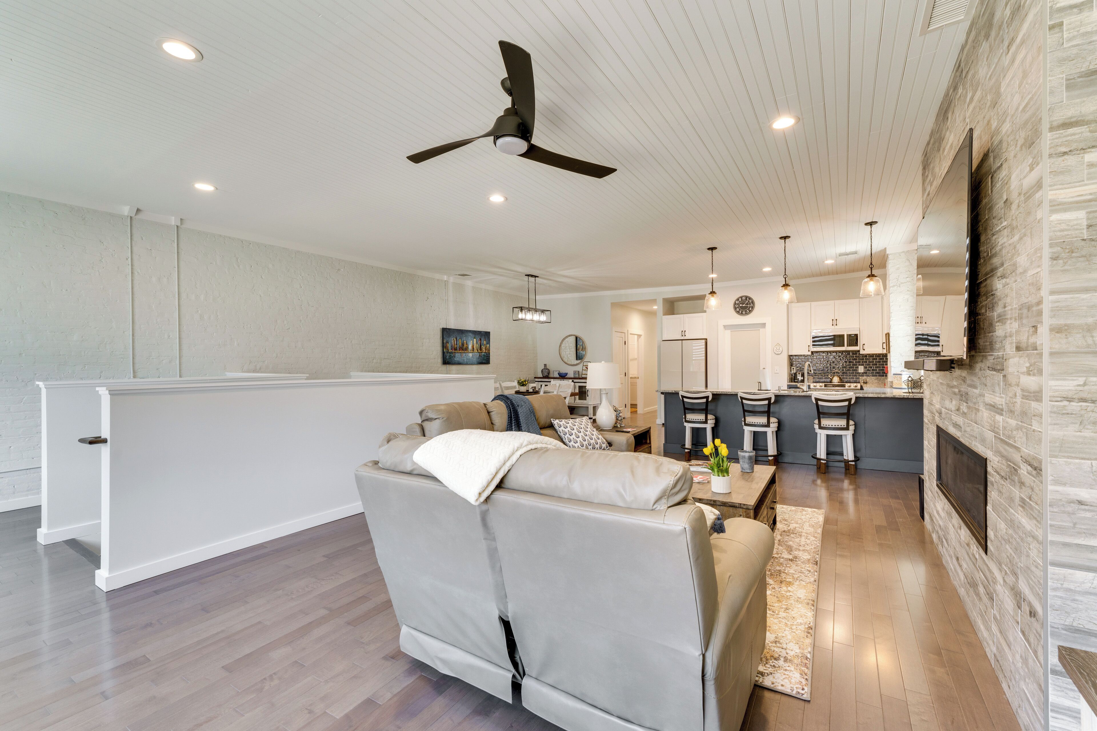 A spacious living room with a sofa, a ceiling fan, recessed lighting, and a kitchen area in the background.