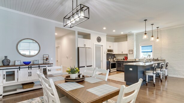 Una cocina moderna con armarios blancos, una isla central con taburetes y un comedor con mesa de madera y sillas blancas.
