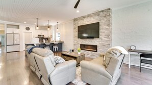 Una sala de estar moderna con chimenea, ventilador de techo y cocina al fondo.