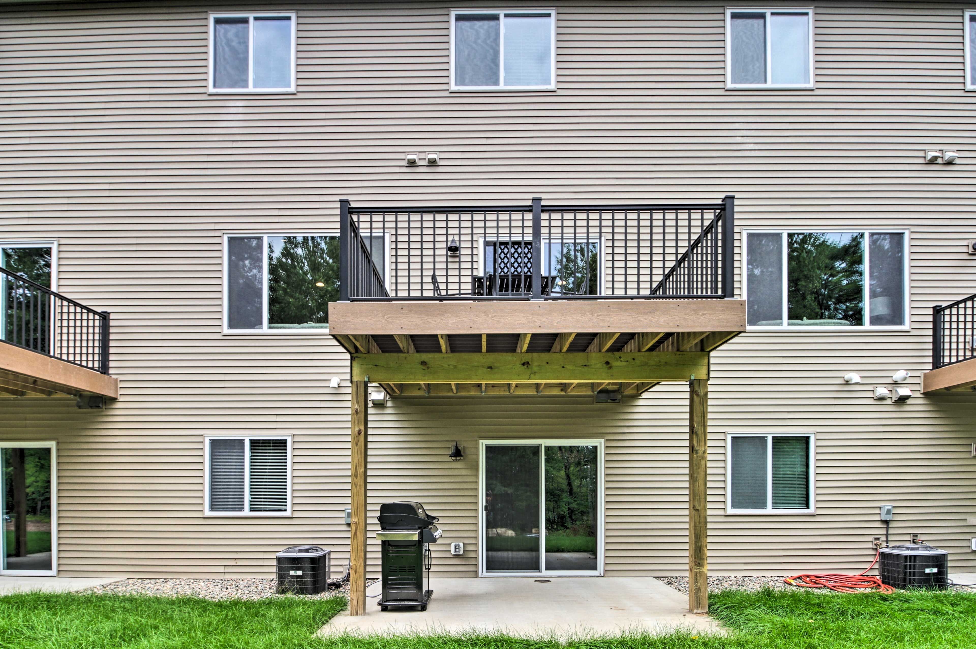 A two-story building with a covered patio area, a grill, and a trash can.