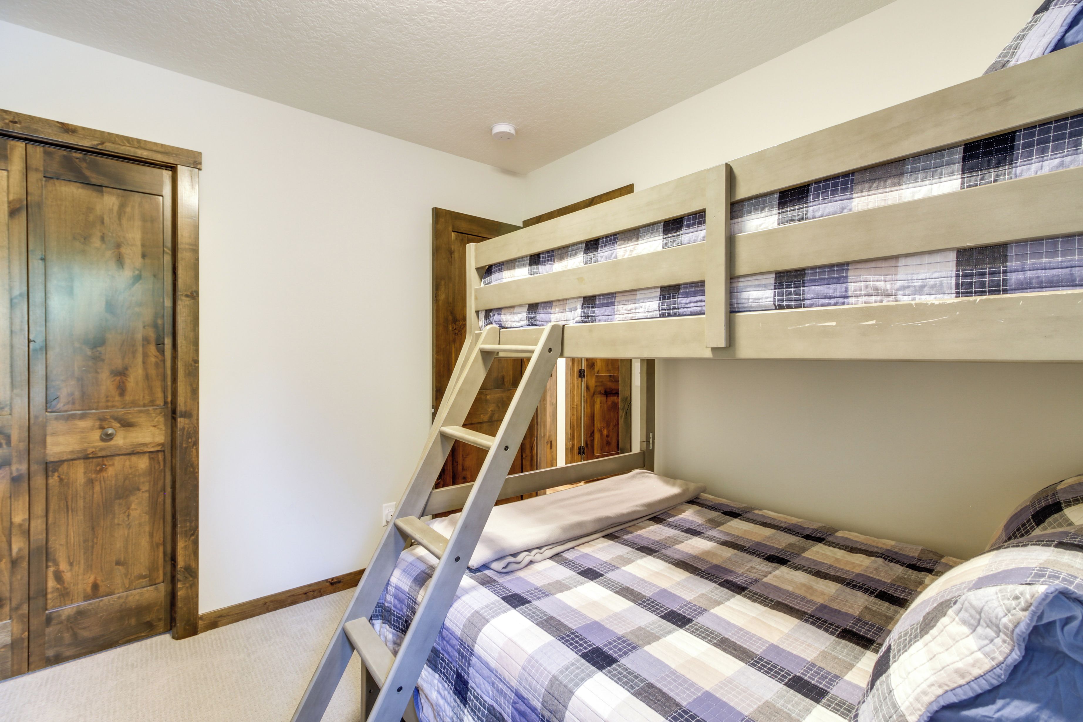 A bunk bed with a ladder, a wooden wardrobe, and a checkered bedspread.