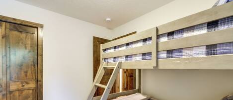 A bunk bed with a ladder, a wooden wardrobe, and a checkered bedspread.