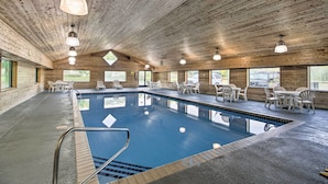 Una piscina interior con paredes y techo de madera, rodeada de sillas y mesas blancas.