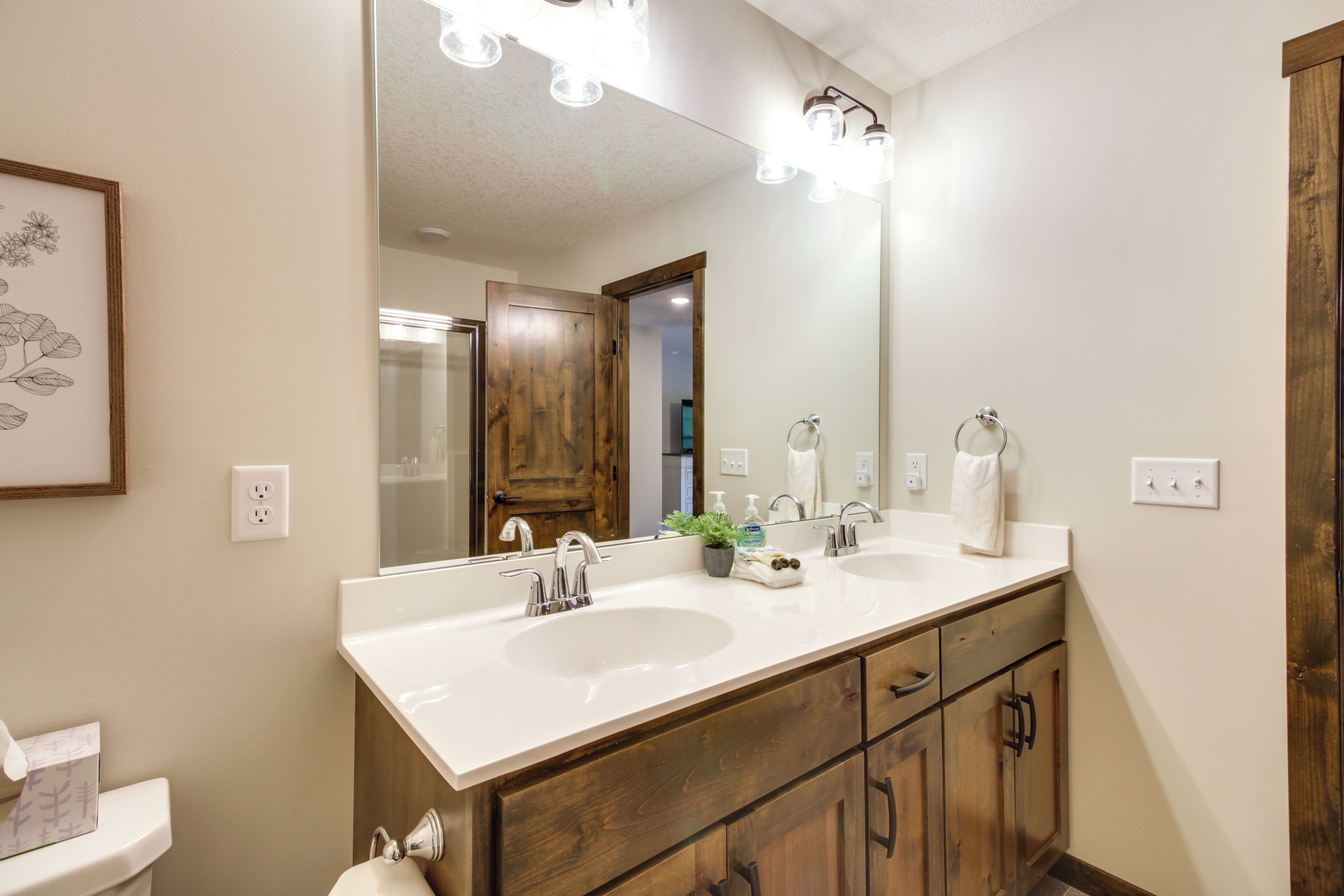 Un bagno con doppio lavabo, mobile contenitore in legno e un grande specchio illuminato.