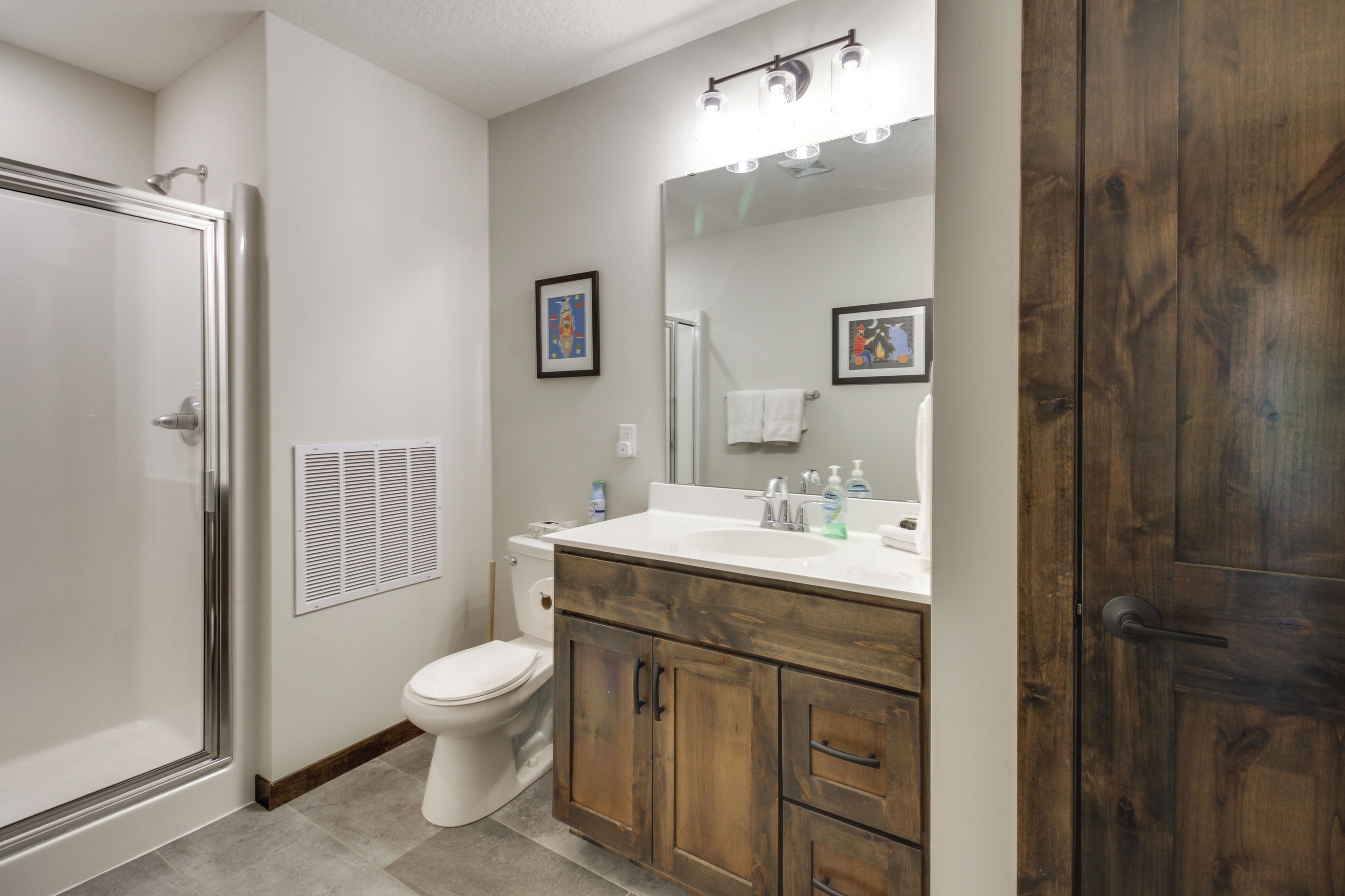 A bathroom with a shower, toilet, vanity with a mirror, and wooden cabinets.