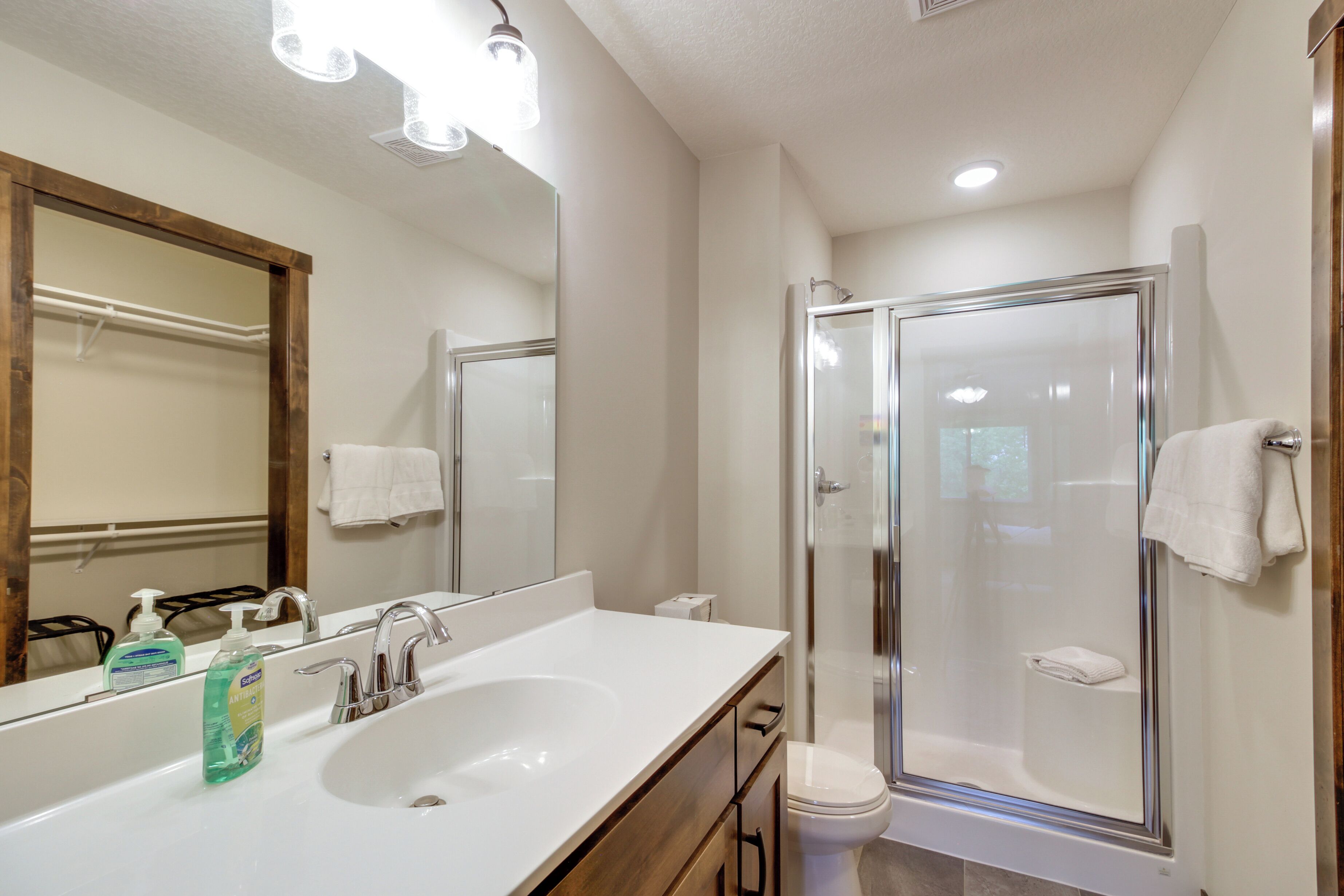 Une salle de bain moderne avec un grand miroir, un lavabo doté d’un distributeur de savon, des toilettes et une douche à parois de verre.