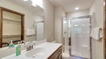 A modern bathroom with a large mirror, a sink with soap dispenser, a toilet, and a glass-enclosed shower.