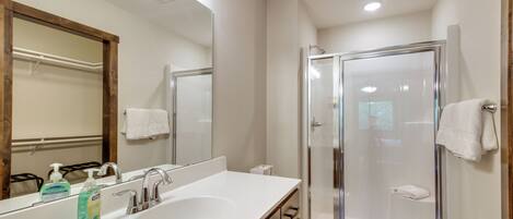 Une salle de bain moderne avec un grand miroir, un lavabo doté d’un distributeur de savon, des toilettes et une douche à parois de verre.