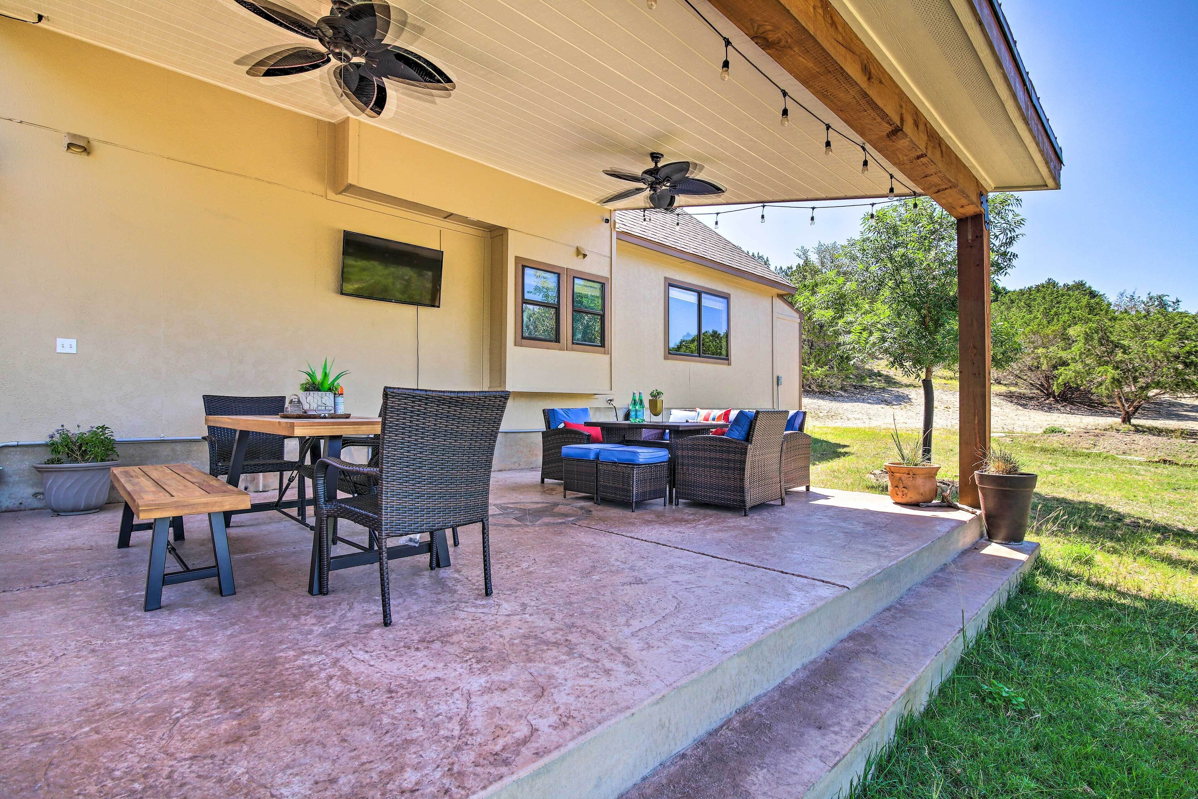 Une terrasse extérieure avec une table et des chaises, un ventilateur de plafond et des plantes en pot.