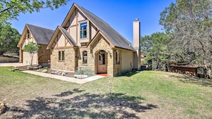 A two-story stone house with a stone chimney, a front porch, and a well-maintained lawn. - Game Room + 1-acre Yard! Lake Travis Retreat (Leander)