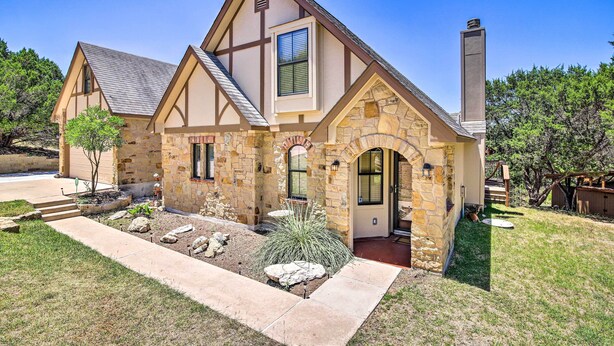 A two-story house with a stone facade, a prominent chimney, and a well-maintained front yard with landscaping. - Game Room + 1-acre Yard! Lake Travis Retreat (Leander)