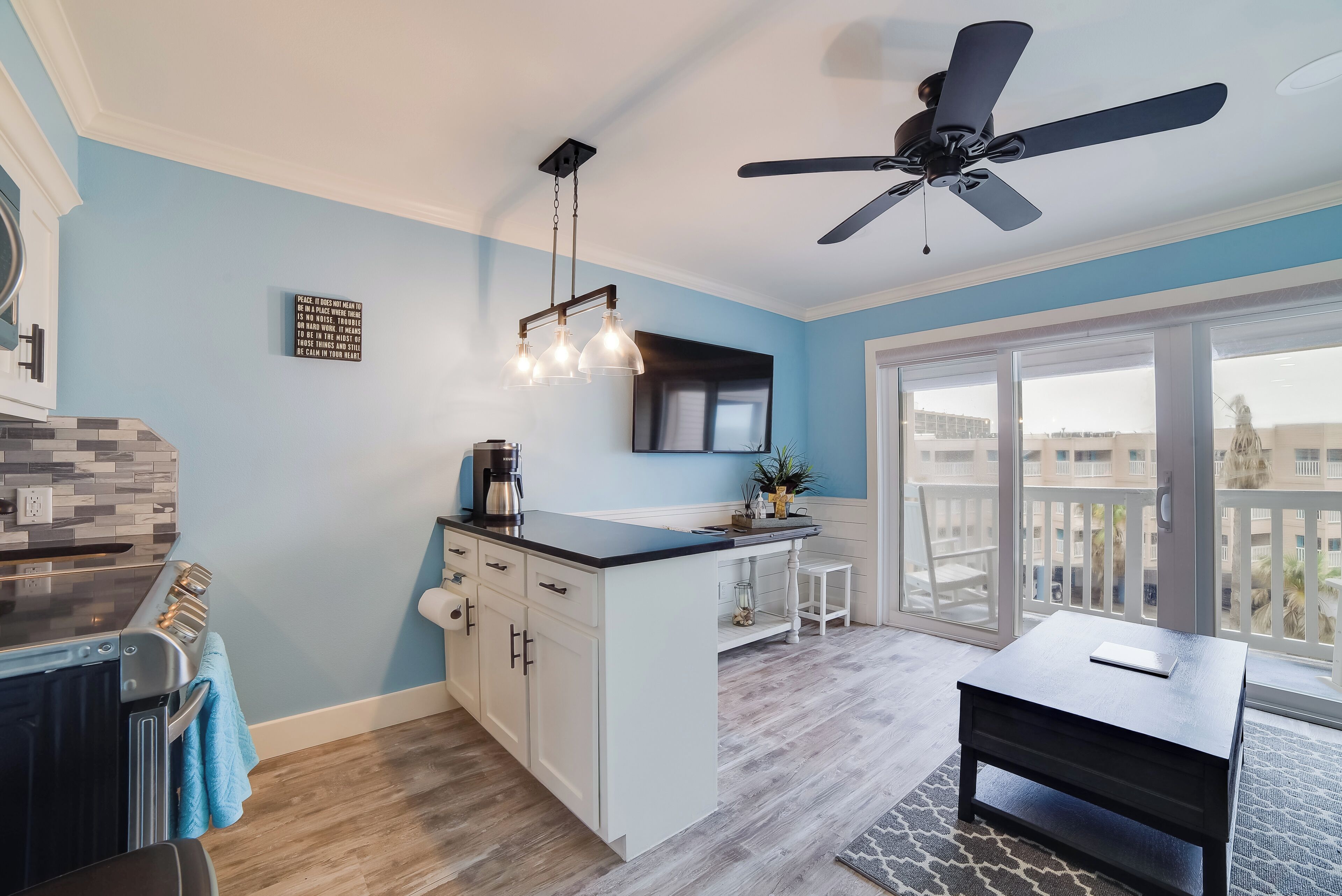 A modern kitchen with a central island, a ceiling fan, and a large window with a view.