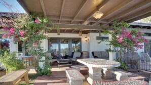 Un patio al aire libre con mesas y bancos de piedra, rodeado de abundante follaje y plantas con flores.
