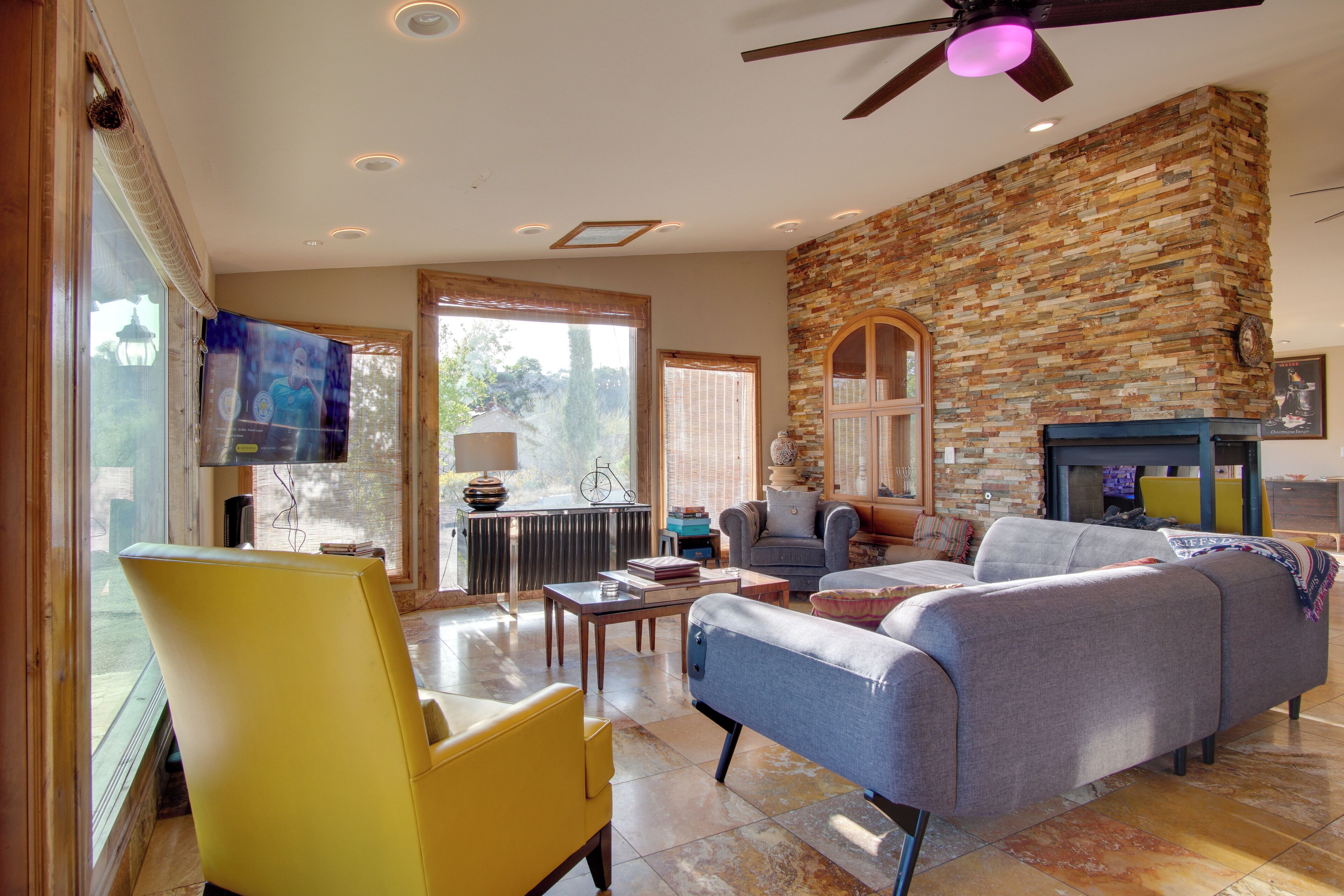 A living room with a stone wall, a ceiling fan, and a television on the wall.