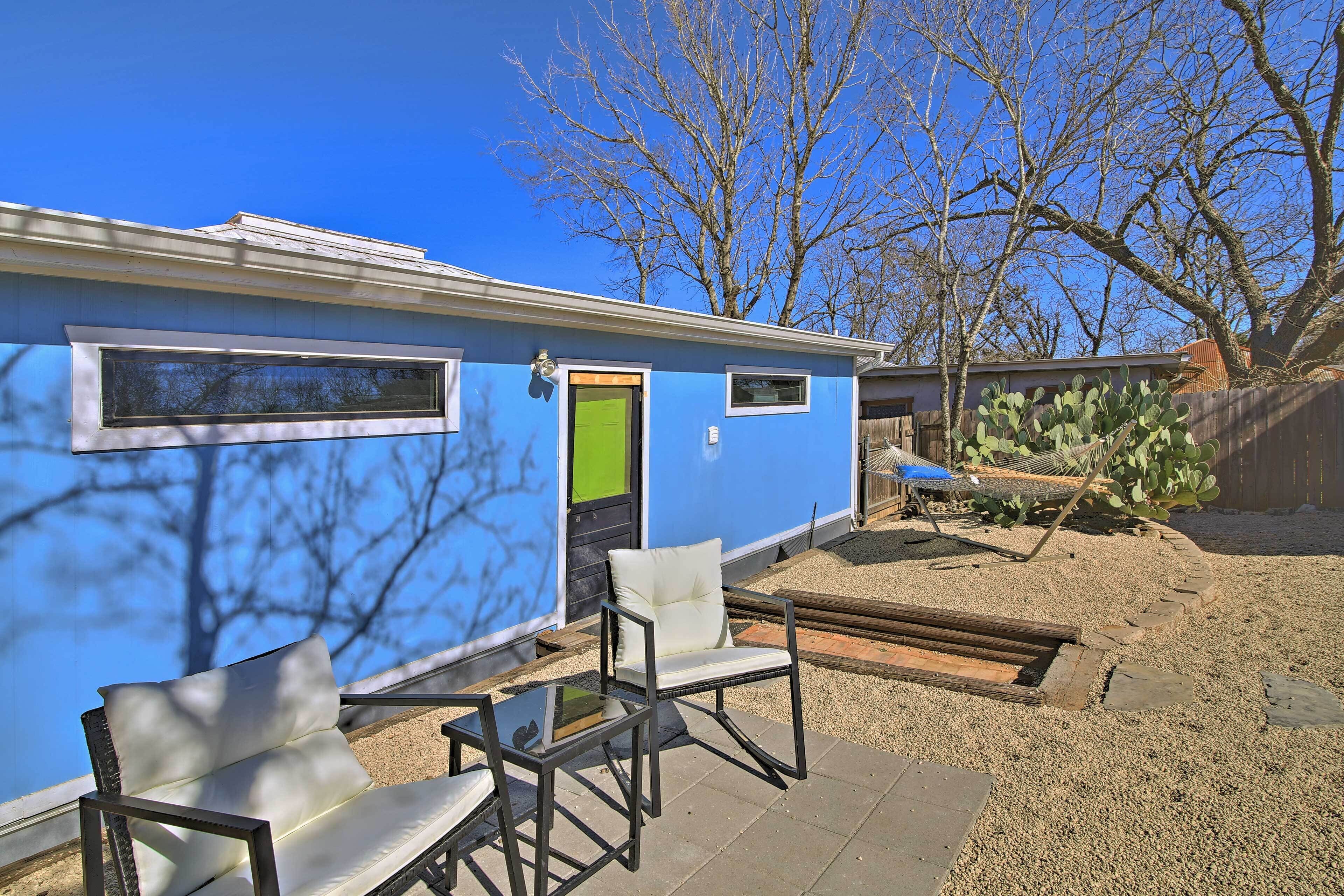 A small, single-story building with a blue exterior, a green door, and a patio area with a table and two chairs.