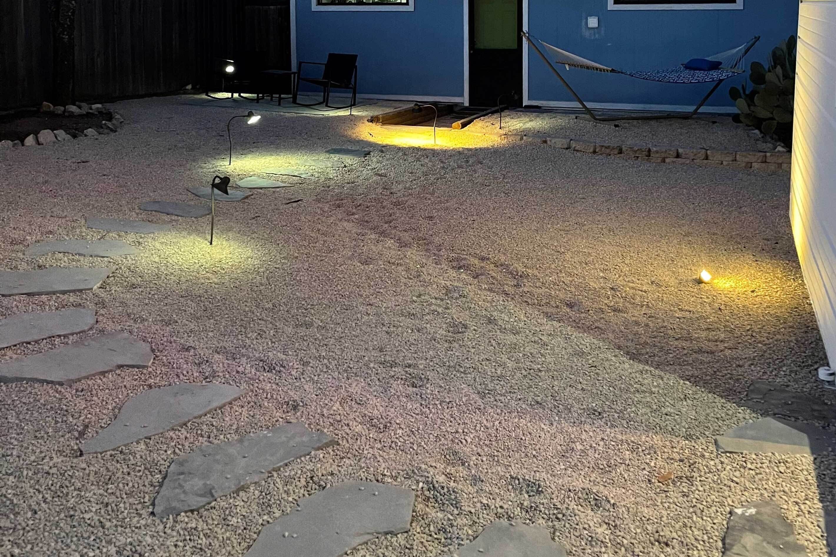 Un patio trasero con un sendero de grava, una hamaca y un área de estar con sillas y una mesa.