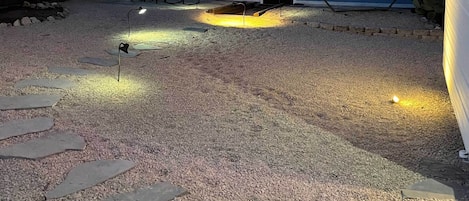 Un patio trasero con un sendero de grava, una hamaca y un área de estar con sillas y una mesa.