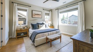 Ein Schlafzimmer mit Bett, Nachttischen, Deckenventilator und großen Fenstern.