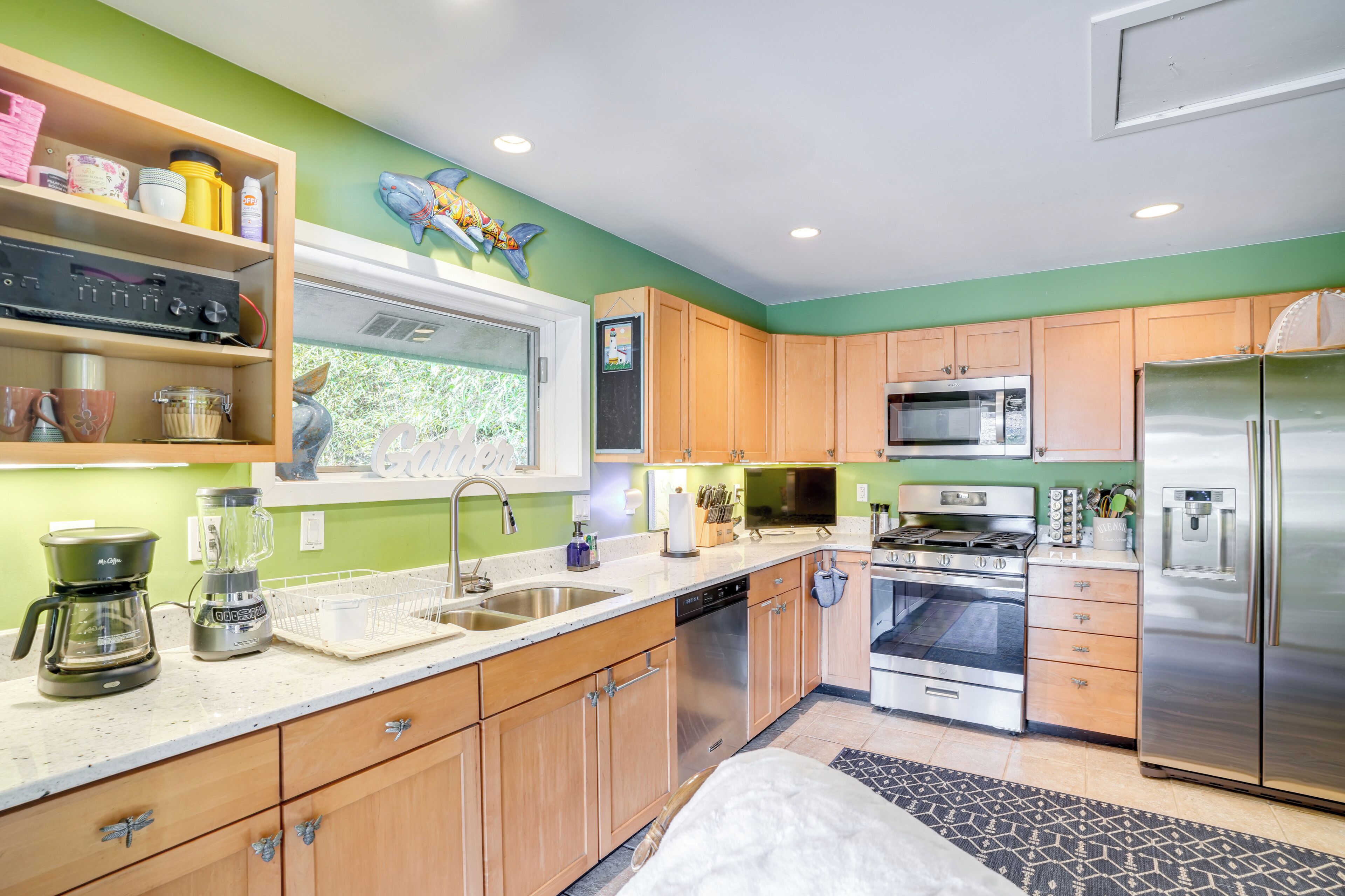 A modern kitchen with wooden cabinets, stainless steel appliances, and a window overlooking greenery.