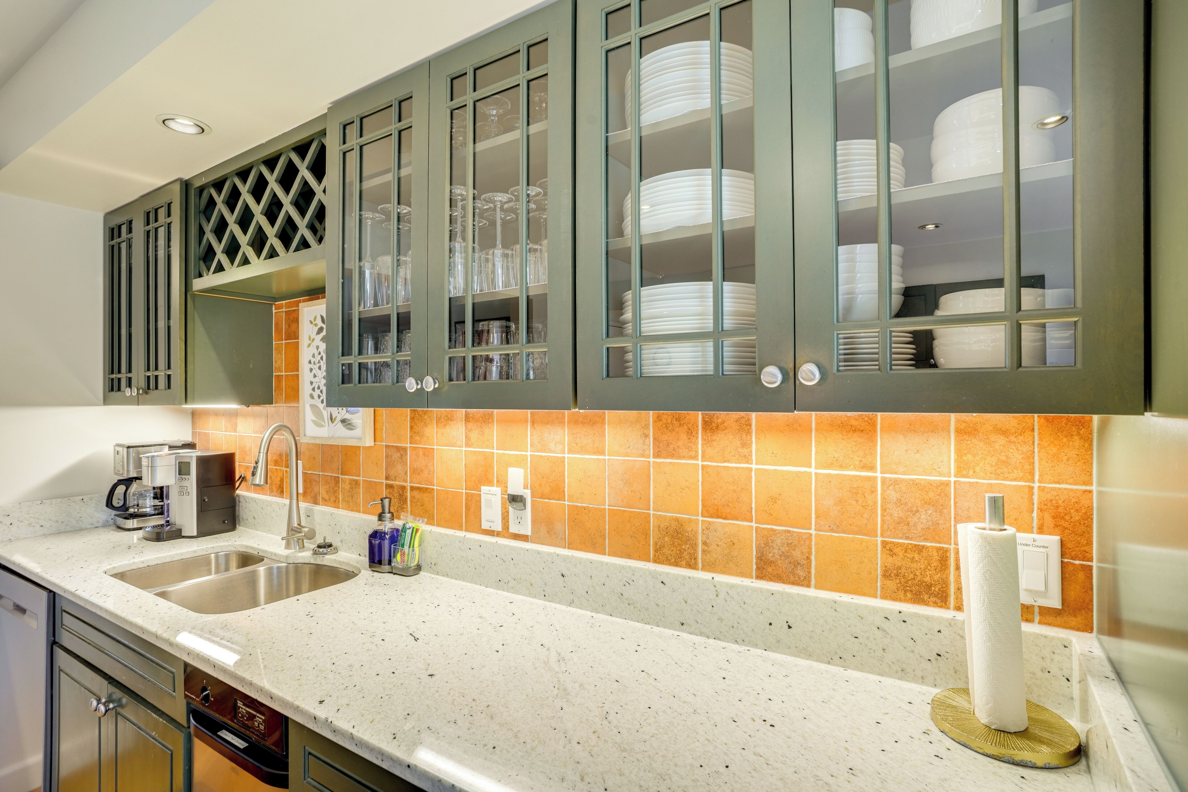 A kitchen with a double sink, stainless steel cabinets, and a backsplash with orange tiles.