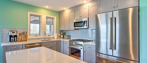 A modern kitchen with stainless steel appliances, a large island, and light green walls.