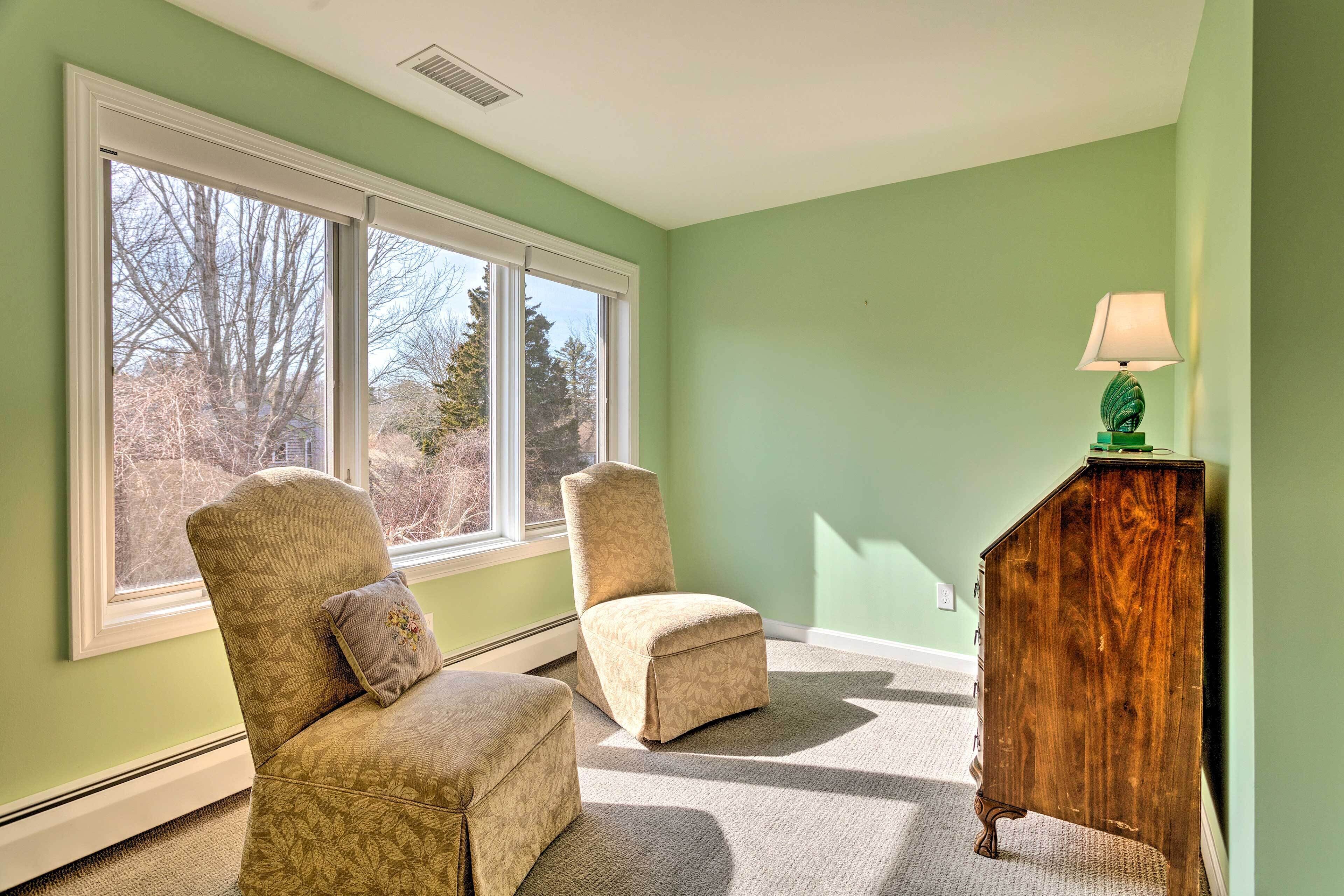 A room with two armchairs, a wooden cabinet, and a window with a view of trees.