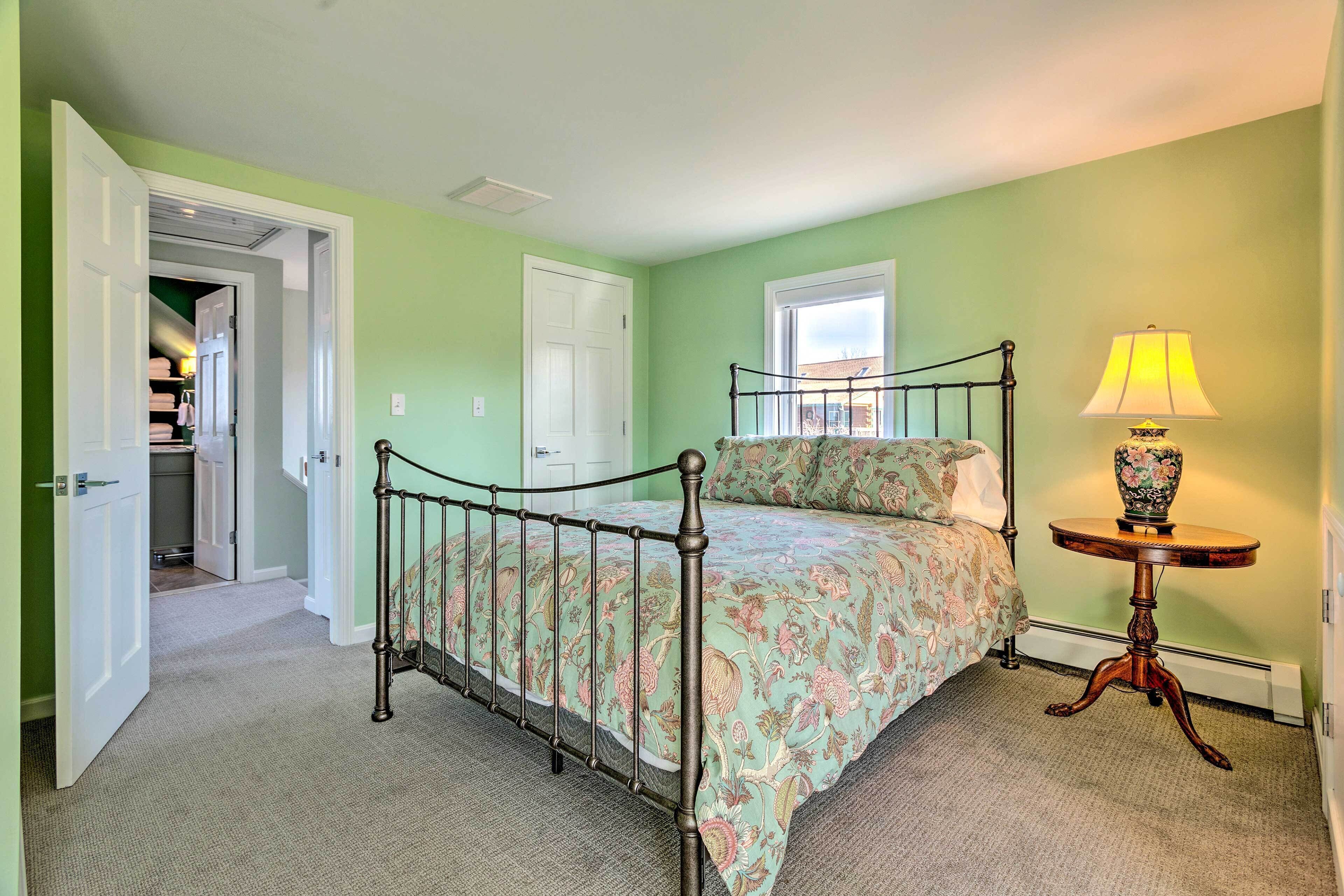 A bedroom with a bed, a nightstand, a lamp, and a door leading to a hallway.