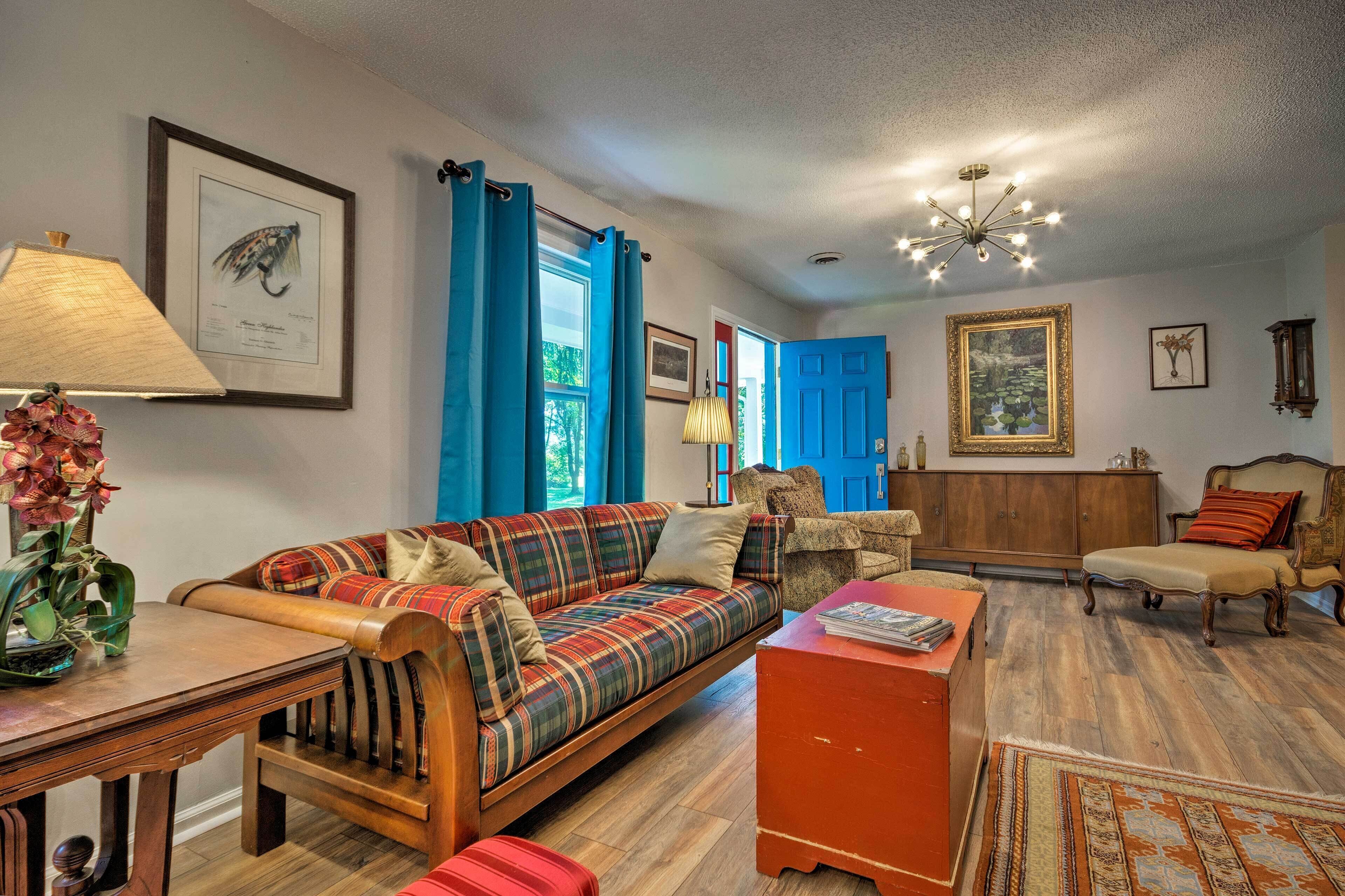 A cozy living room with a sofa, a wooden coffee table, a red ottoman, and a patterned rug.